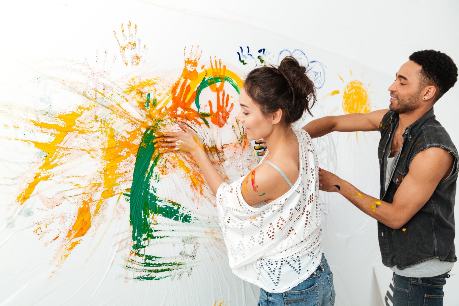 Smiling young couple painting on white wall by hands and colorful paints